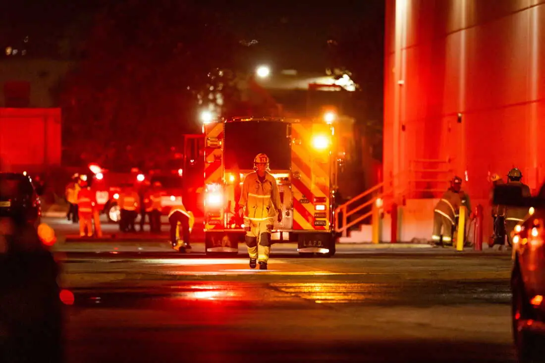 Brandweerlieden van de Los Angeles Fire Department bij brandweerwagens op straat, s nachts verlicht door zwaailichten