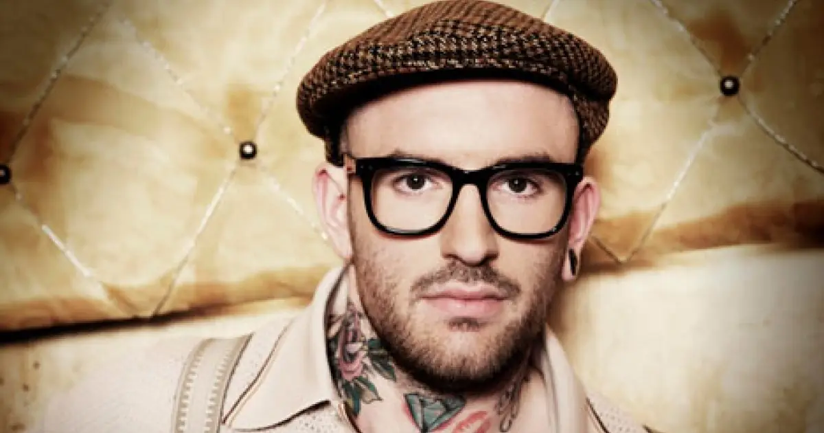 Portret van zanger Ben Saunders met een pet, bril en zichtbare tatoeages in zijn nek