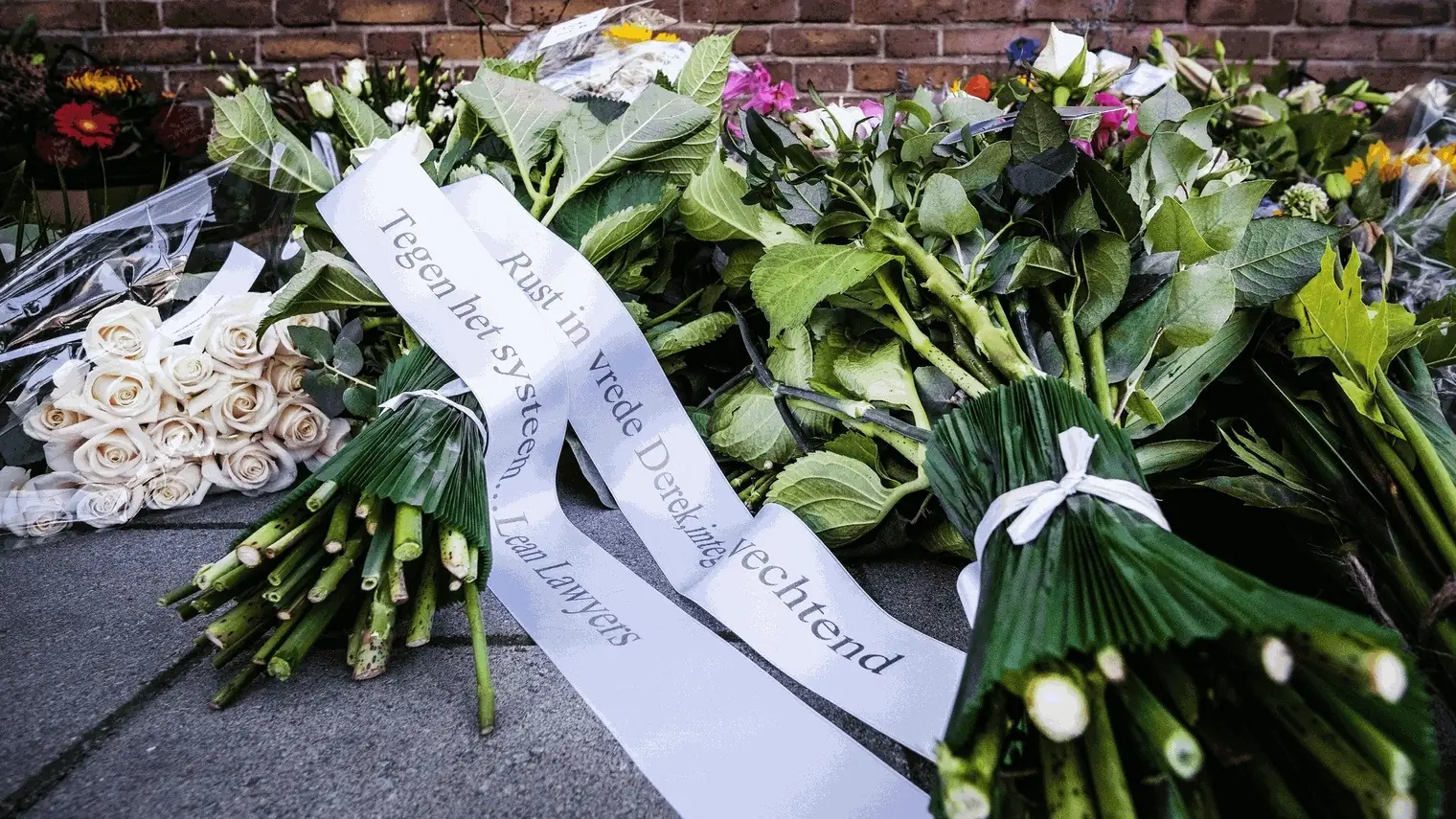 Bloemen en linten met rouwboodschappen voor advocaat Derk Wiersum, neergelegd bij een bakstenen muur