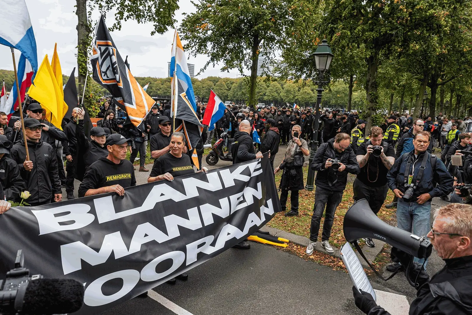 Demonstranten houden een spandoek met de tekst "Blanke mannen vooraan" omhoog, omringd door vlaggen en persfotografen